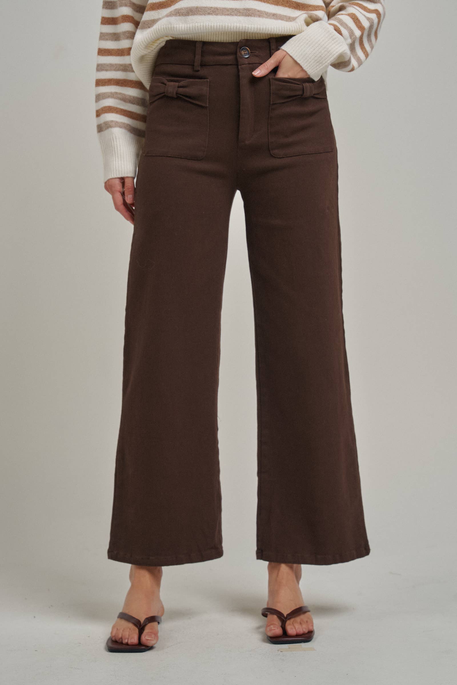 Brown wide leg stretch pants featuring decorative bow front pockets, high waist, and flared cropped hem.